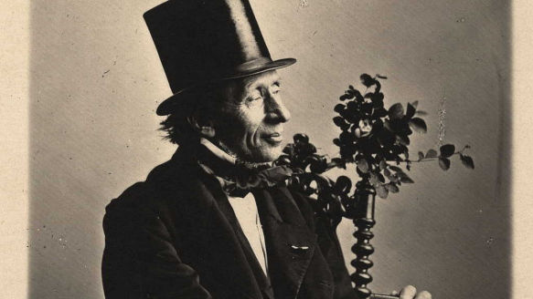 Sort-hvidt foto af H.C. Andersen med høj hat, halvt i profil, siddende med en buket blomster